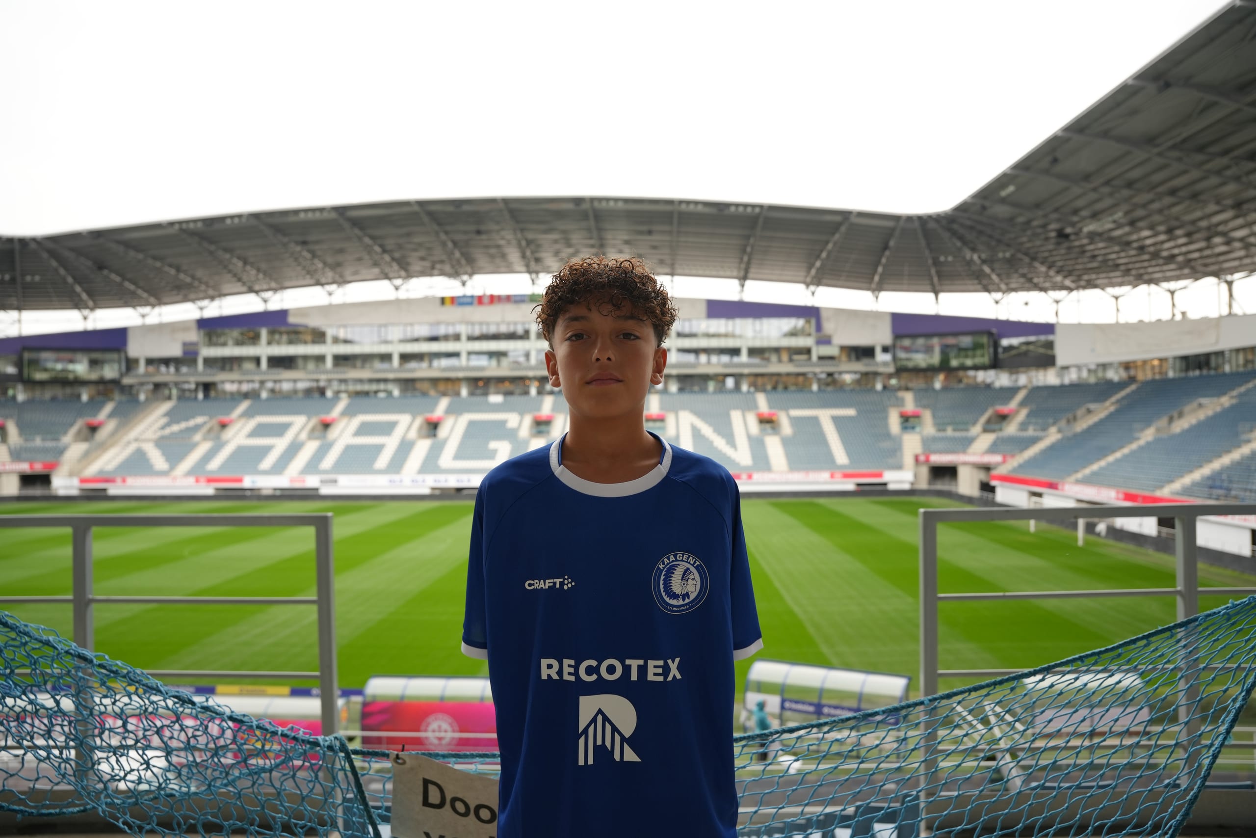 Een jeugdspeler van KAA Gent in het shirt met het Recotex-logo, met het stadion op de achtergrond